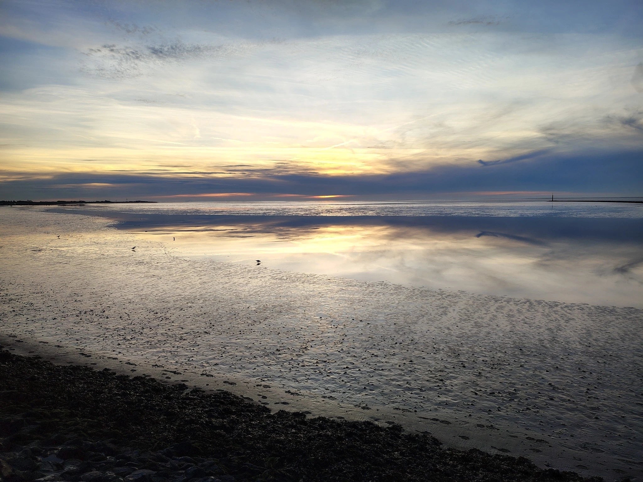 Stimmungsvoller Sonnenuntergang über dem spiegelnden Wattenmeer in Neßmersiel an der Nordsee bei Ebbe.