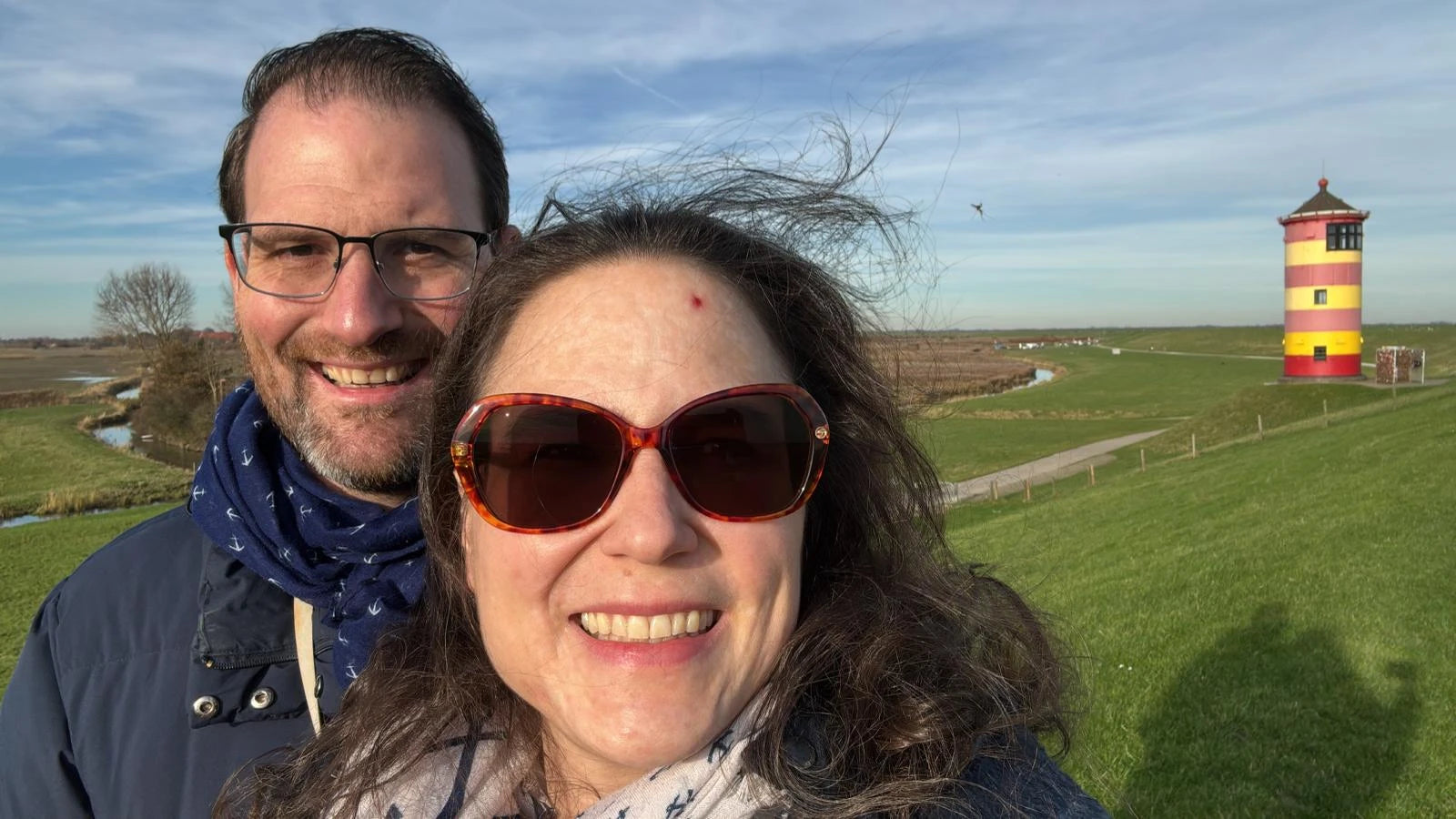 Die Gastgeber des Ferienhauses Strandräubernest Neßmersiel lächelnd bei einem Ausflug am Pilsumer Leuchtturm auf dem Deich in Ostfriesland.