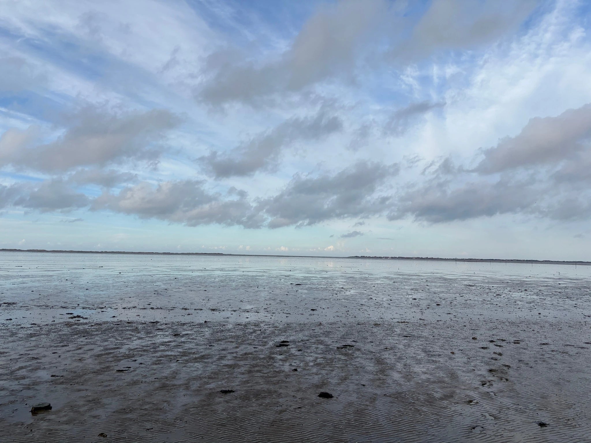 Freigelegter Meeresboden bei Ebbe im UNESCO-Weltnaturerbe Wattenmeer in Neßmersiel an der Nordsee unter weitem Wolkenhimmel.
