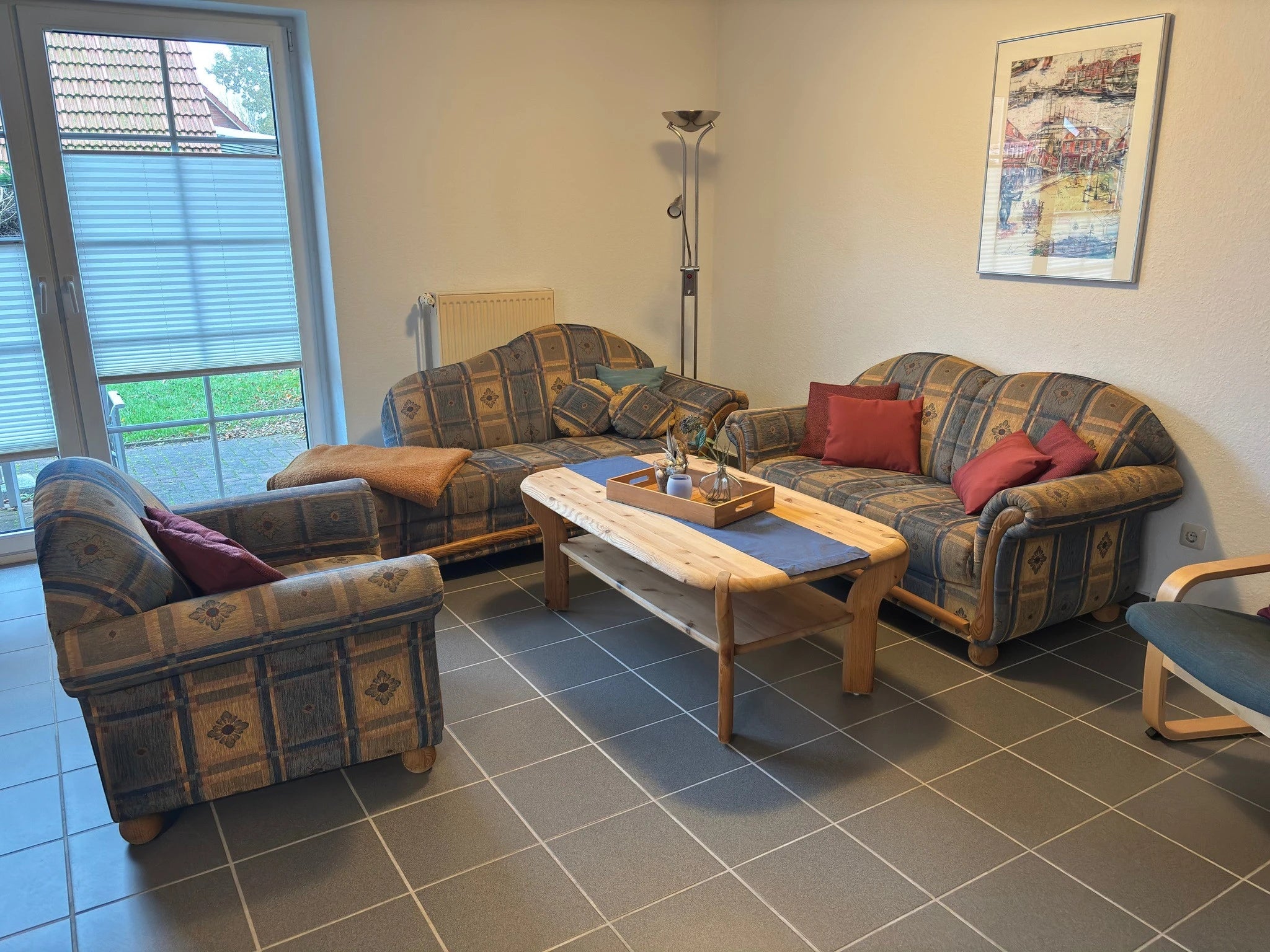 Gemütliche Sitzecke im Wohnzimmer des Ferienhauses Strandräubernest Neßmersiel mit zwei Sofas, einem Sessel, Holztisch und direktem Blick auf die Terrasse.