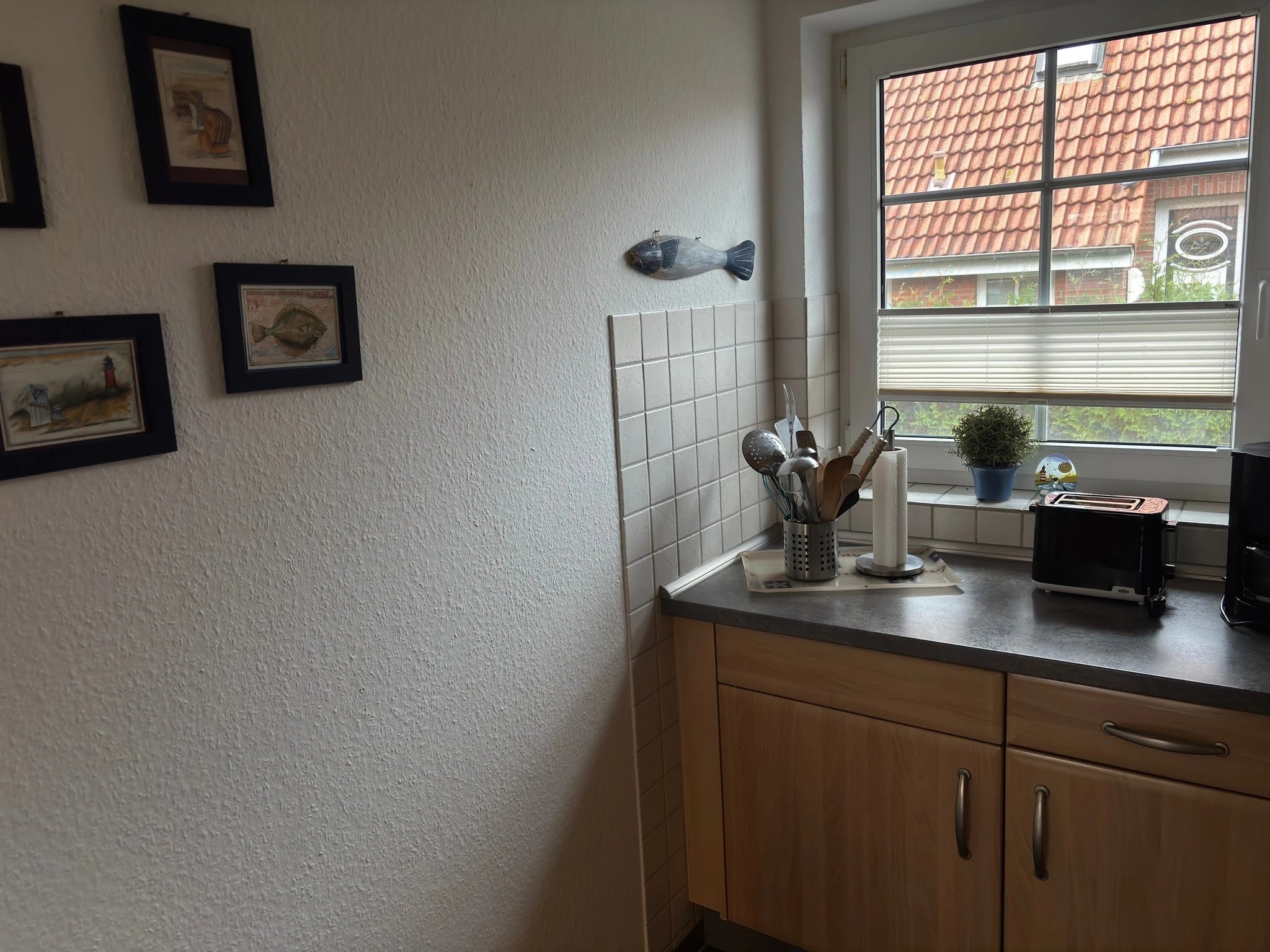 Helle Küche im Ferienhaus Strandräubernest Neßmersiel mit Toaster, Küchenutensilien, Arbeitsplatte und maritim dekorierten Wandbildern am Fenster.